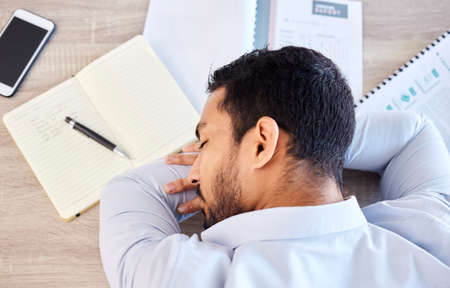Businessman sleeping on a table from above. Tired young man having a nap on his desk at work in a...