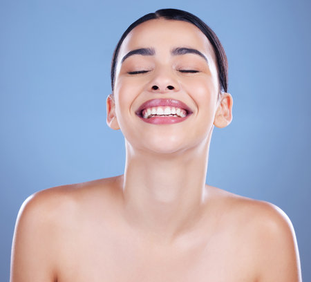 Happy makes me beautiful. an attractive young woman posing alone against a blue background in the studio.の写真素材