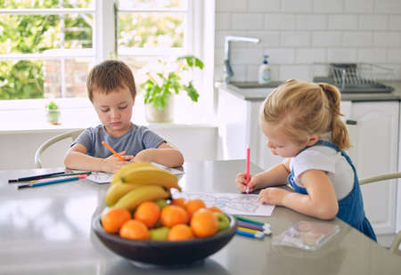 Caucasian siblings drawing pictures together. Brother and sister doing homework. Children colouring...