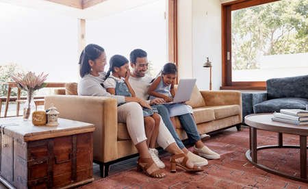 Lets see whats happening on the web. Full length shot of an affectionate young family of four using a laptop while sitting on the sofa at home.の写真素材