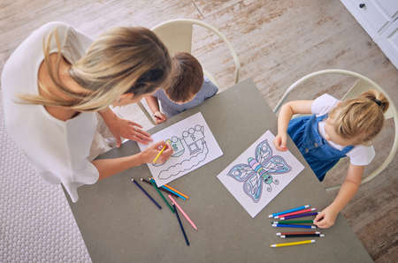 Above shot of little girl and boy sitting at table with colourful pencils and pictures while...