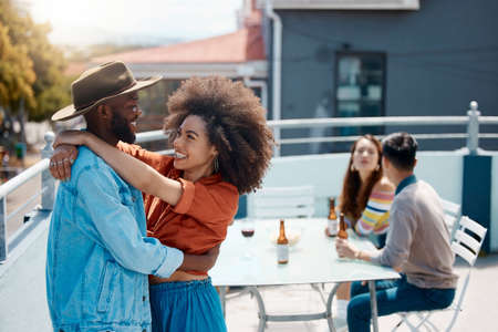 Happy interracial couple hugging while spending time together outside at a restaurant with friends....