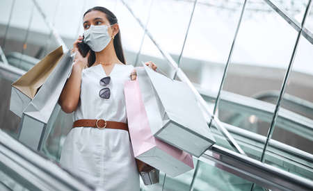 One young mixed race woman wearing a medical face mask and talking on a cellphone while on an...