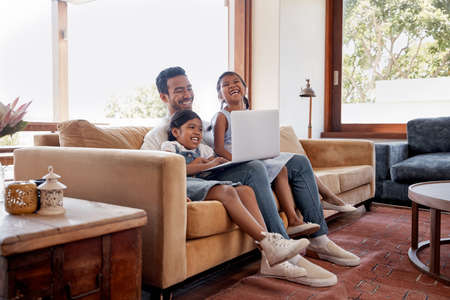 Lazy laptop days. Full length shot of a handsome young man and his two daughters using a laptop while sitting on the sofa at home.の写真素材