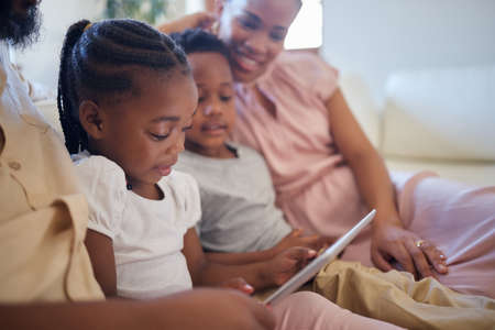 A young african american family sitting on the sofa together and smiling while using a tablet at homeの写真素材