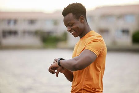 A man looking at his watch and smiling. An African America man in sportswear waiting and smiling at his smartwatch.の写真素材