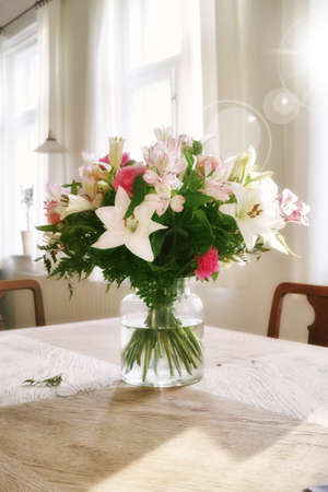 Vibrant bunch of blossoms displayed for interior decoration. Colorful bouquet in a vase on a table at home with lens flare. Fresh peruvian and easter lily flowers blooming with green foliage.の写真素材