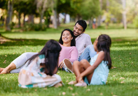 Portrait of happy asian couple lying together on grass. Kids playing while watching their loving parents spending time together at the parkの写真素材