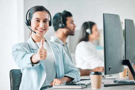 For service thats rated five stars. Portrait of a young call centre agent showing thumbs up while working in an office with her colleagues in the background.の写真素材