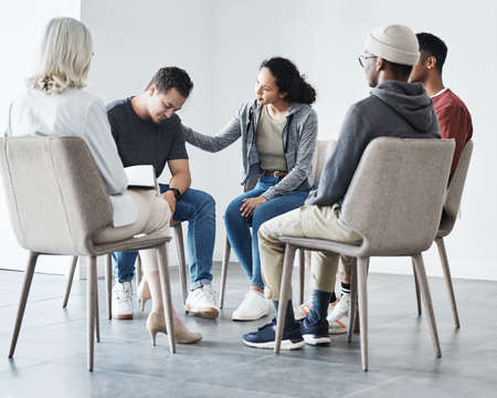 Man having a breakdown during group therapy session about addiction. Friend giving support to...
