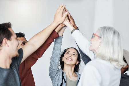 Diverse group of people standing together in circle and raising their hands in middle after therapy for a high five. Smiling support group celebrating successful session. Friends support mental healthの写真素材