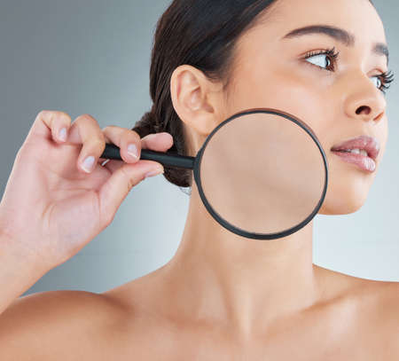 Examine your skin. an attractive young woman posing in studio against a grey background.の写真素材