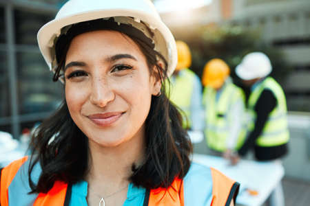 Ive got a capable team behind me. an attractive young contractor standing outside while her colleagues work behind her.の写真素材