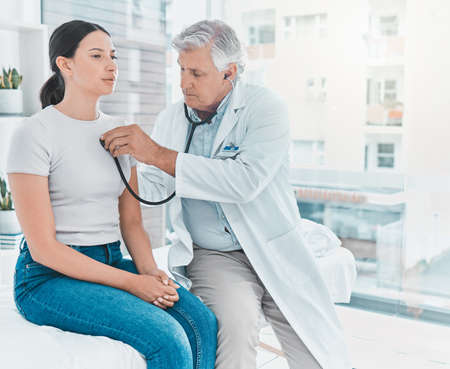 Breathe in and out for me. a doctor listening to a patients heartbeat using a stethoscope.の写真素材