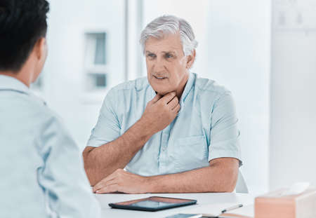 Ive been experiencing pain in my throat. a mature man sitting with his doctor and complaining about a sore throat during a consultation.の写真素材