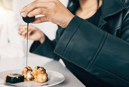 Just a little something to sweeten the deal. a woman pouring soy sauce onto her sushi.の写真素材