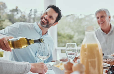 A strong family has well worn seats at the table. a male pouring wine during lunch at home.の写真素材