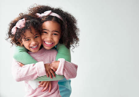 Our baby girls are so adorable from head to toe. two adorable little girls hugging and standing together against a grey background.の写真素材