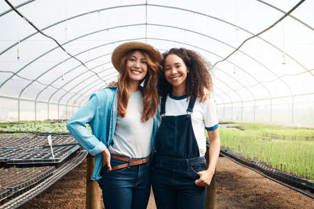 Weve got this farm running smoothly. Cropped portrait of two attractive young woman standing in a greenhouse on a farm.の写真素材