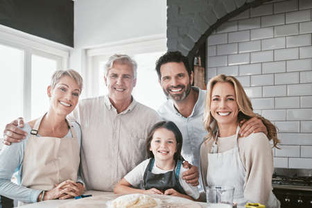 . Happy smiling caucasian family baking together in the kitchen. Little cheerful girl helping her parents and grandparents bake. Senior woman and man cooking with their family.の写真素材