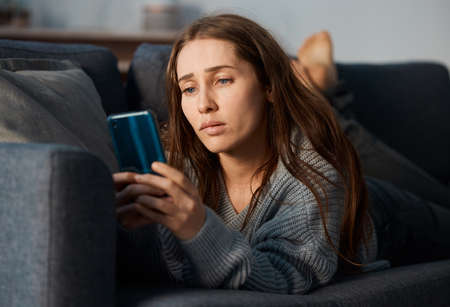 She cant stop checking. a young woman looking depressed while using her smartphone.