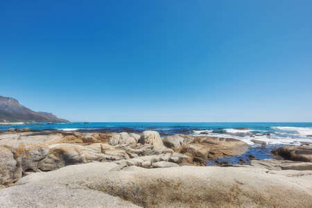 Copy space ocean view of beach with rocks, boulders and sea water washing onto rocky shore on...