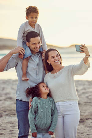Happy cheerful mixed race family smiling for a selfie spending time at the beach together. Hispanic...
