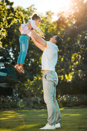Happy family. Young mixed race father playing with his little daughter lifting her up while they...