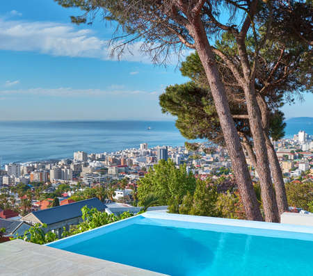 A blue pool on a luxury property with a coastal view of Cape Town and tourist landscape. The ocean and city against a clear sky horizon. A popular travel destination for tourists in South Africaの写真素材