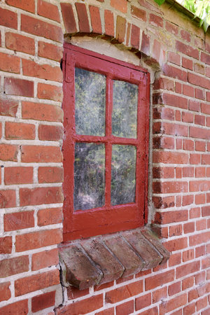 Old dirty window in a red brick house or home. Decaying casement with redwood frame on a historic building with clumpy paint texture. Exterior details of a windowsill in a traditional town or villageの写真素材
