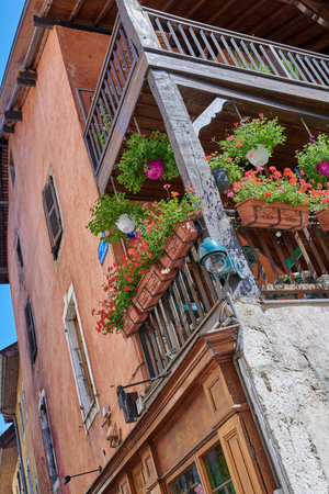 A building in a beautiful old town with flowers growing in the outdoors. Developing architecture and balcony. View of plants in a villa house and street life in the famous city of Annecy, France.の写真素材