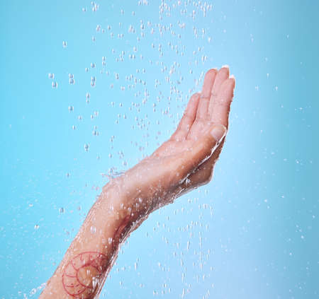 She loves being under the water. Studio shot of an unrecognizable young woman showering against a blue background.の写真素材