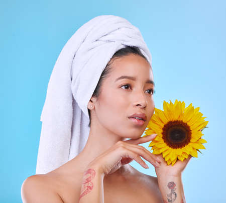 As bright and fresh as a sunflower. Studio shot of an attractive young woman posing with a towel on her head and a sunflower in her hand against a blue background.の写真素材