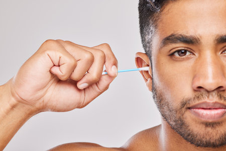 Maybe itll improve my hearing. a young man cleaning his ears against a grey background.
