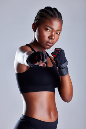 Shes more powerful than you think. Studio portrait of a sporty young woman wearing gloves and punching against a grey background.の写真素材