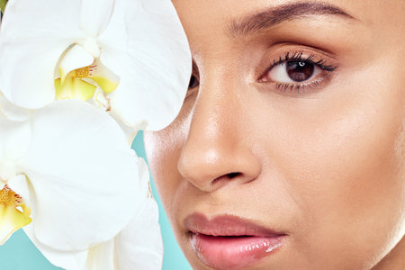 Like a flower her beauty blooms. a beautiful young woman covering her face with an orchid against a studio background.の写真素材