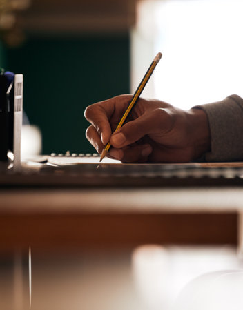. Closeup of students hand using a pencil to write notes at a table. One clever guy studying for...