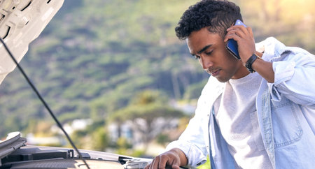 Im looking under the hood now. a handsome young man on the phone with roadside assistance after...