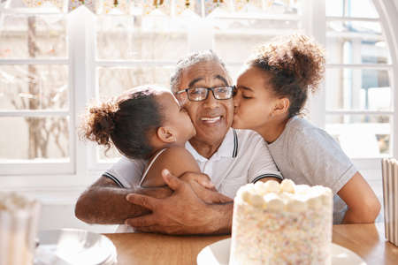 Time flies like an arrow. two Grand daughters kissing their grandpa during a birthday party at home.の写真素材