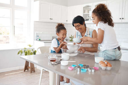 Pour slowly for a fine mixture. a mature woman baking with her granddaughters.の写真素材