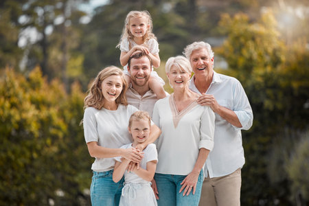 Portrait of a smiling multi generation caucasian family standing close together in the garden at home. Happy adorable girls bonding with their mother, father, grandfather and grandmother in a backyarの写真素材