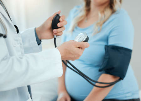 We care about your health and the health of your growing child. a doctor using a blood pressure gauge during a checkup with his pregnant patient.の写真素材