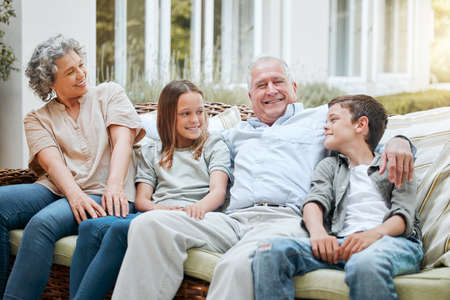 We have both of our grandchildren with us. a senior couple sitting outside with their two grandchildren.の写真素材