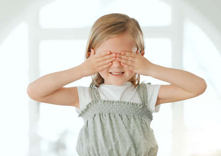 I dont want to watch. an adorable little girl standing alone at home and covering her eyes with her hands.の写真素材