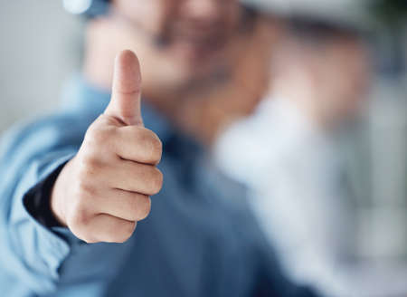 Closeup shot of an unrecognisable call centre agent showing thumbs up in an office.の写真素材