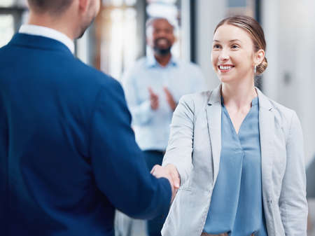 Lets shake on that. two businesspeople shaking hands in an office at work.
