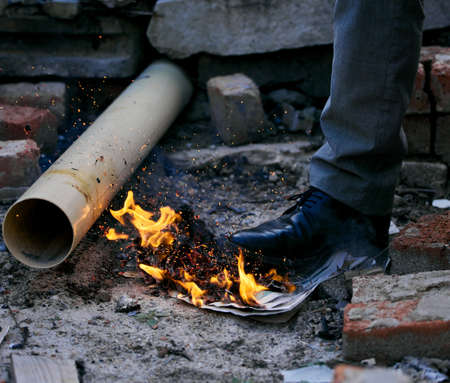 Playing with fire is bad for those who burn themselves. a unrecognizable man stepping on a burning paper inside a burned down house.の写真素材