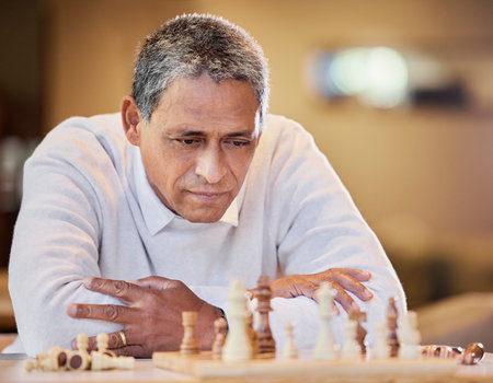 My opponent is really good. a mature man sitting alone inside and looking contemplative while playing a game of chess.の写真素材
