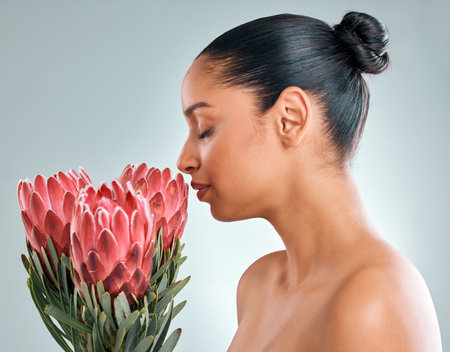Smells so beautiful, smells like me. Studio shot of an attractive young woman smelling protea flowers against a grey background.の写真素材