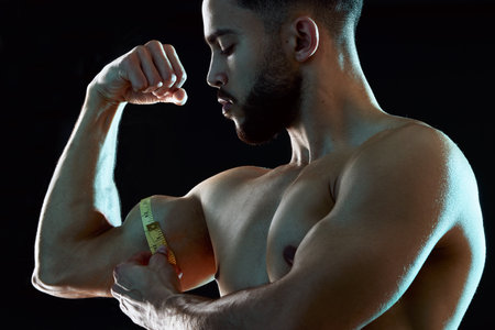 Gains like these dont grow on trees. Studio shot of a fit young man measuring his bicep against a dark background.の写真素材